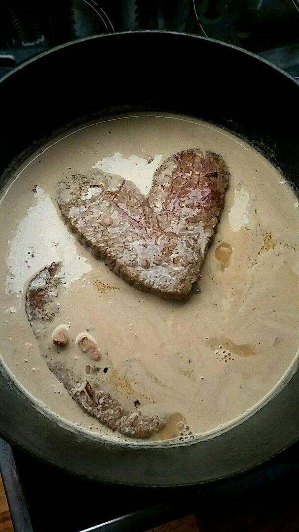 A heart shaped piece of meat in a cream sauce in a dark, black pan